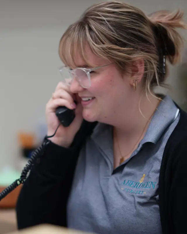 A receptionist smiling while on the phone at the Aberdeen Surgery front desk