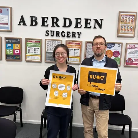Two more team members holding R U OK? Day posters under the Aberdeen Surgery sign